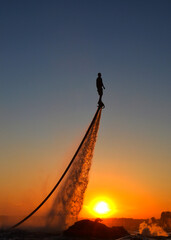 The new spectacular sport, the flyboard is showed in the coast of beach on the sunset. Man on flyboard