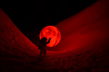 Silhouette of the toy of astronaut against levitating glowing sphere over surface icy planet...