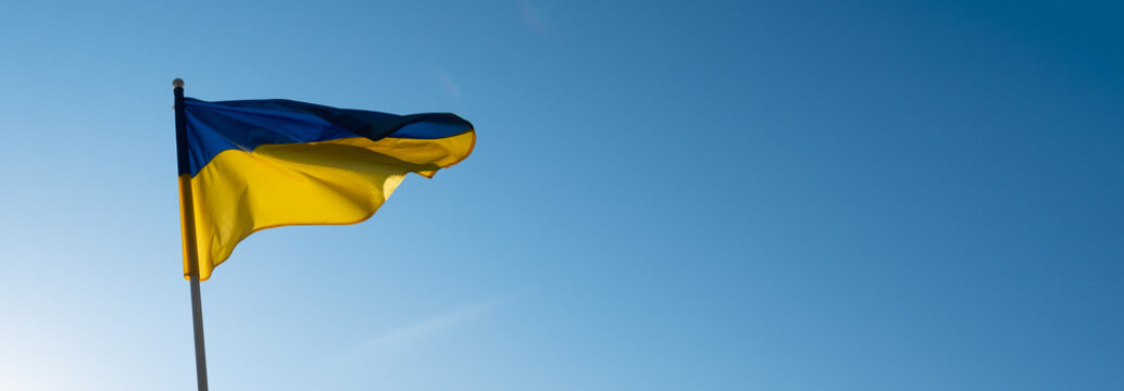 Ukrainian flag banner with empty copy space. Flag of Ukraine on blue sky background. National symbol of freedom and independence. "Slava Ukraini!" (Glory to Ukraine).