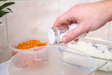 A man pours spices and salt into minced meat in a bowl for lazy cabbage rolls on the table.