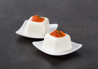 Cream cheese jelly in the shape of a small French square savarin, with red caviar, on a serving...