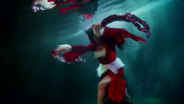 Christmas festival underwater, woman with tinsel is swimming inside pool, celebrating winter fest