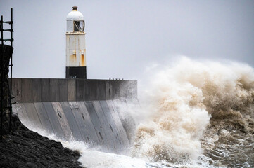 Huge ocean waves crashing into a sea wall and lighthouse Porthcawl, South Wales, UK Storm Eunice
