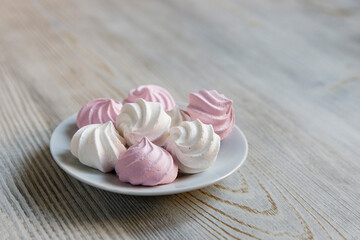 White and pink marshmallows on a white saucer on a beige table