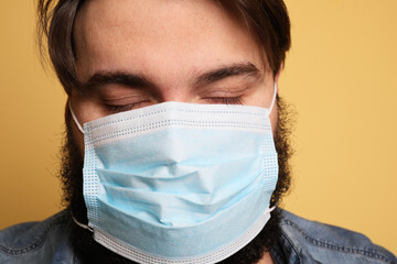 Cropped photo of overweight young man wearing medical face mask on yellow wall.