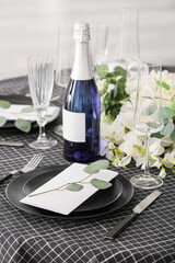 Stylish table setting with wedding invitation and bottle of champagne