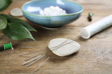 Stone with acupuncture needles on wooden table