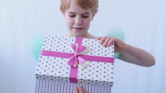 A teenage girl in a beautiful evening dress. The child opens the box with the gift. The emotions of surprise and happiness from the surprise in the box