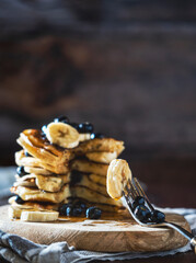 Piece of baked American pancakes with blueberries, banana and honey syrup on a rustic wooden board. Delicious and healthy dessert for breakfast.