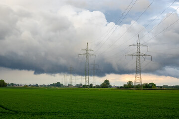 Two seemingly endless rows of electricity pylons in a meadow against cloudy sky