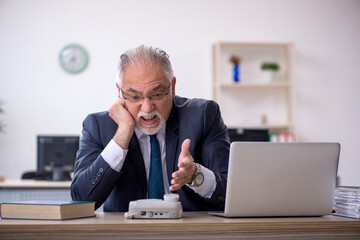 Old male employee speaking on the phone at workplace