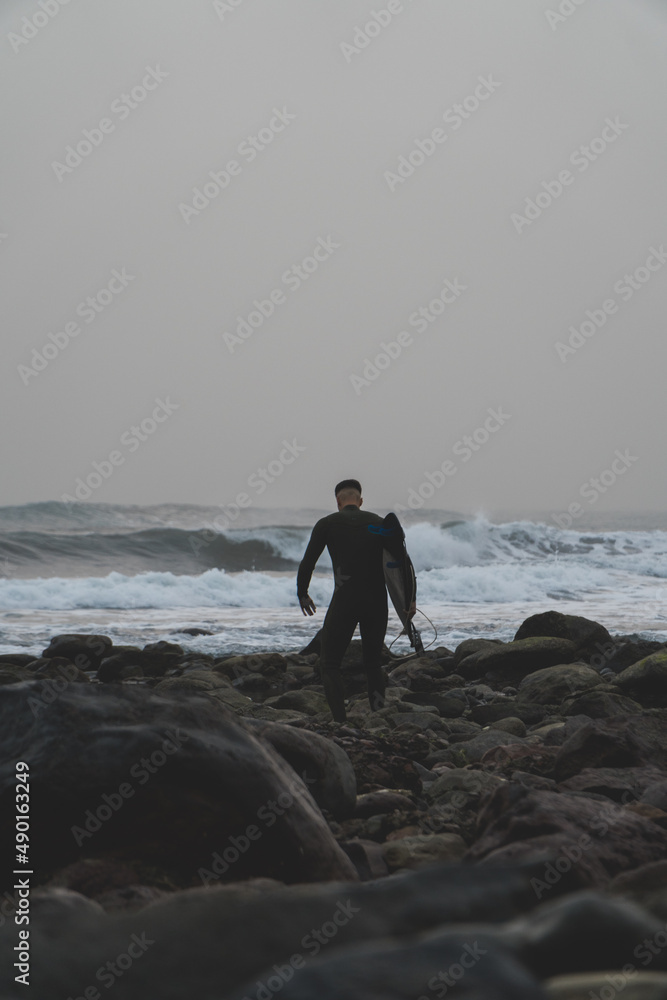 Canvas Prints View of a young surfer holding surf board on the beach at sunset