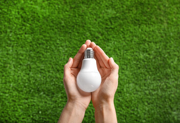 Woman holding LED light bulb over green grass, top view