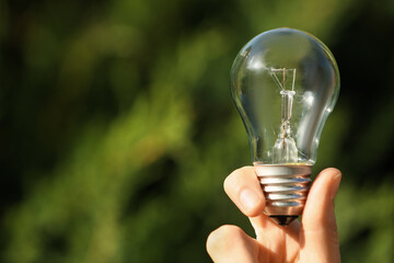 Woman holding incandescent light bulb on blurred green background, closeup. Space for text