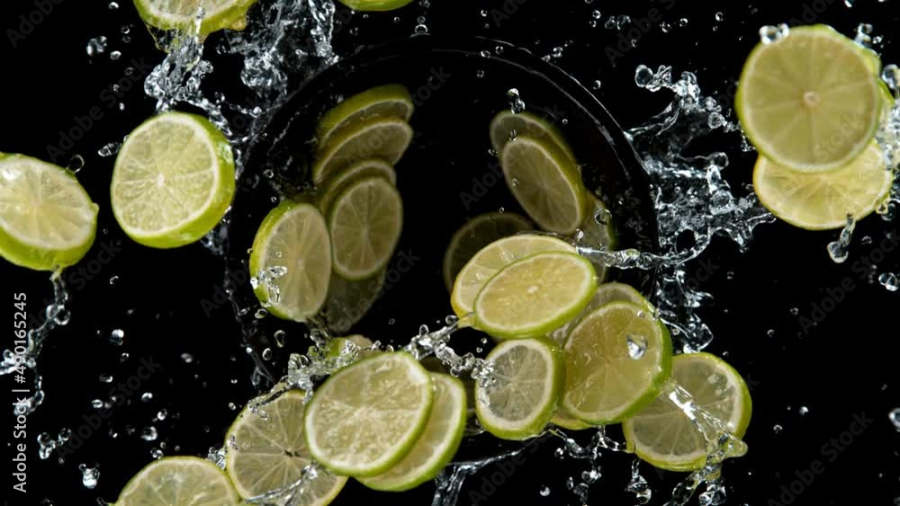 Fototapete super slow motion of rotating lime slices with splashing water, black background. filmed on high spe