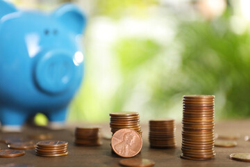 Many metal coins and piggy bank on wooden table against blurred green background. Space for text