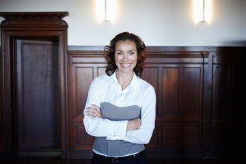 Shes a positive influence in the courtroom. Cropped shot of an attractive female laywer standing with her arms folded and smiling widely in the courtroom.