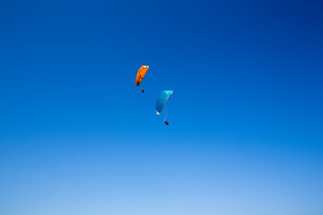 Two paragliders flying one orange and the other blue over a very clean cloudless sky