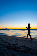 Fototapeta na wymiar Silhueta de mulher caminhando na praia no fim de tarde mexendo no celular