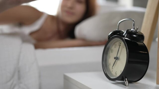 Young woman continues to sleep after turning off alarm clock in morning.