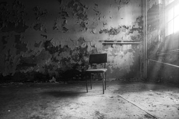 Grayscale view of an old chair in an empty room in an abandoned place