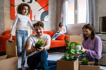 Group of people small caucasian girl helping their parents to pack or unpack stuff from the boxes while moving in to the new apartment taking care of plants real people family man woman with children