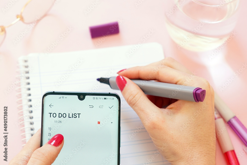 Poster Closeup shot of a woman holding a smartphone and writing down her 