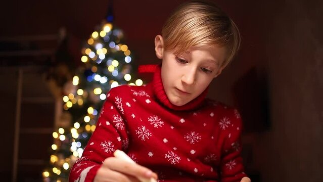 a child in a red sweater draws with markers on the background of Christmas lights