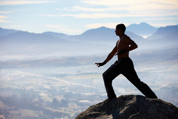 Mountain training is the best. A male kickboxer high up on a mountain top to practice.