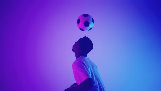 african footballer is kicking up ball by heads in studio, doing keppie uppie, skill for field player