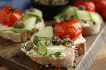 Fototapeta na wymiar Bruschettas with capers, vegetables and cream cheese served on wooden board, closeup