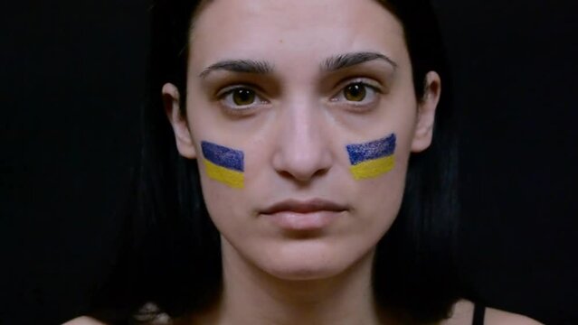 Portrait of young girl with blue and yellow ukrainian flag on her cheek looking at a camera. HD video footage
