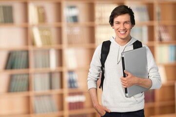 Portrait of cheerful student with backpack, learning accessories standing near bookshelves at library