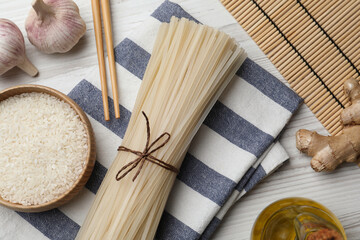 Fototapeta na wymiar Bowl with dried rice noodles and ingredients on white wooden table, flat lay