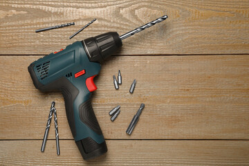 Modern electric power drill with different bits on wooden table, flat lay. Space for text