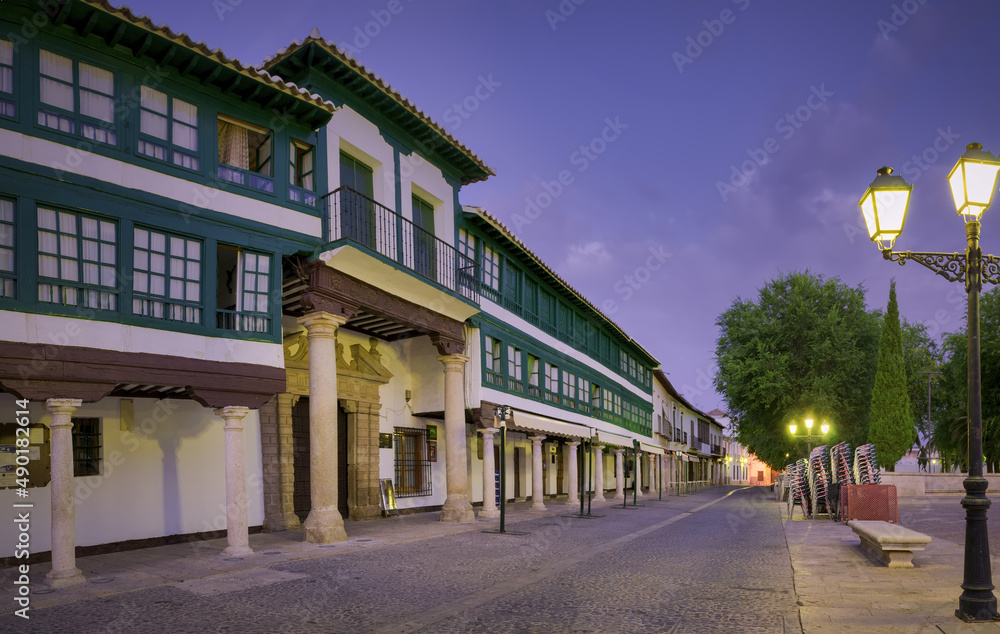 Poster scenic view of a paved and illuminated street with columns in the evening
