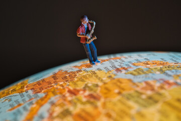 Miniature saxophonist on a globe with dark background. front view . Concept: world music tour