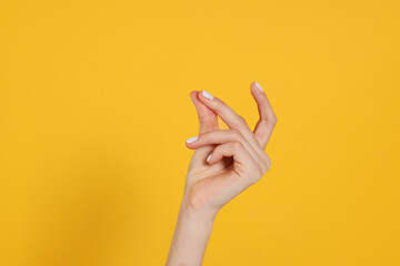 Woman snapping fingers on yellow background, closeup of hand
