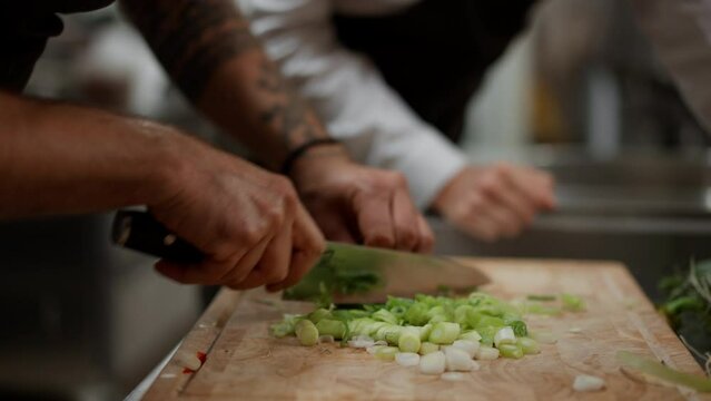 Unrecognizable chef cutting vegetables indoors in restaurant kitchen.