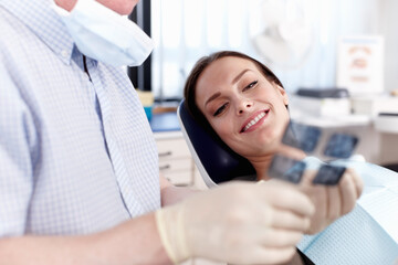 Doctor explaining x-ray to female patient. Portrait of dentist showing x-ray to female patient in clinic.