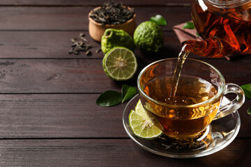 Pouring bergamot tea into glass cup at wooden table. Space for text
