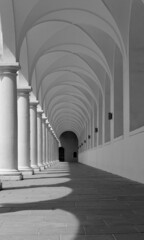Grayscale of an arched hallway with sunlight coming through the white columns