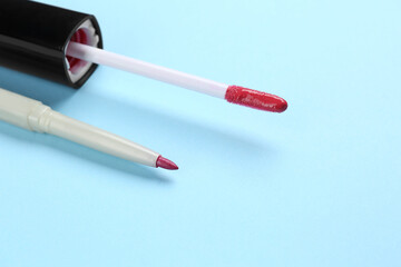 Lip pencil and brush of liquid lipstick on light blue background, closeup. Cosmetic product