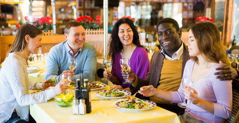 Group of joyous friends enjoying evening meal at cozy restaurant