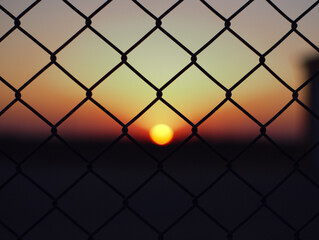 Closeup of chain-link fences in a field with the sunset in the blurry background