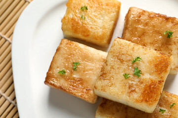 Ceramic plate with delicious turnip cake on bamboo mat, closeup