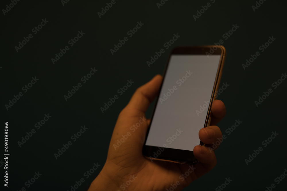 Poster closeup of a hand holding a phone with white blank space on display on a dark background