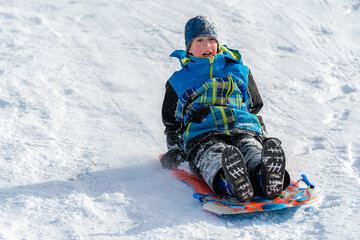 Fototapeta na wymiar Boy Sledding Down Hill on Snow