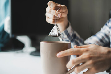 person's hand holding a tea bag and making hot cup of tea