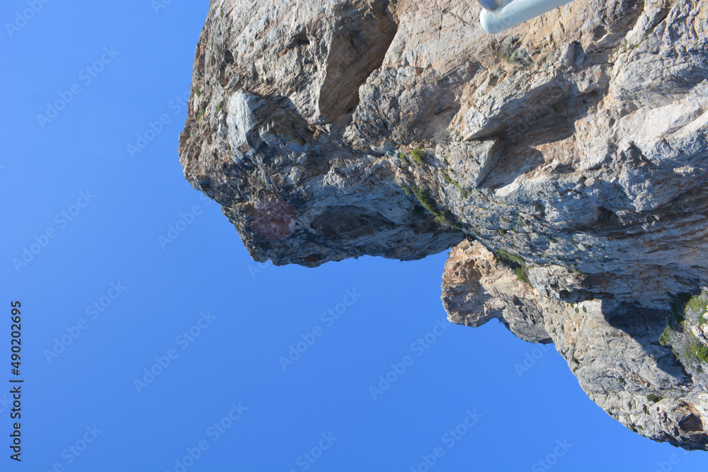 Sticker Low-angle shot of the peak of a rock or cliff against the clear blue sky in summer